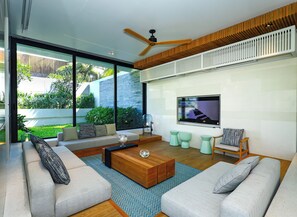 A modern living room with a large TV, comfortable seating, and a view of a garden.