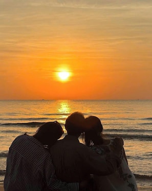 Een zonsondergang boven de zee, met een koppel en een kind zittend op het strand.