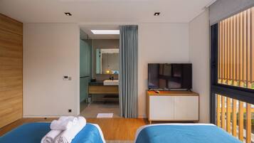 Habitación de hotel con dos camas, televisión, escritorio y baño visible a través de una puerta de cristal.
