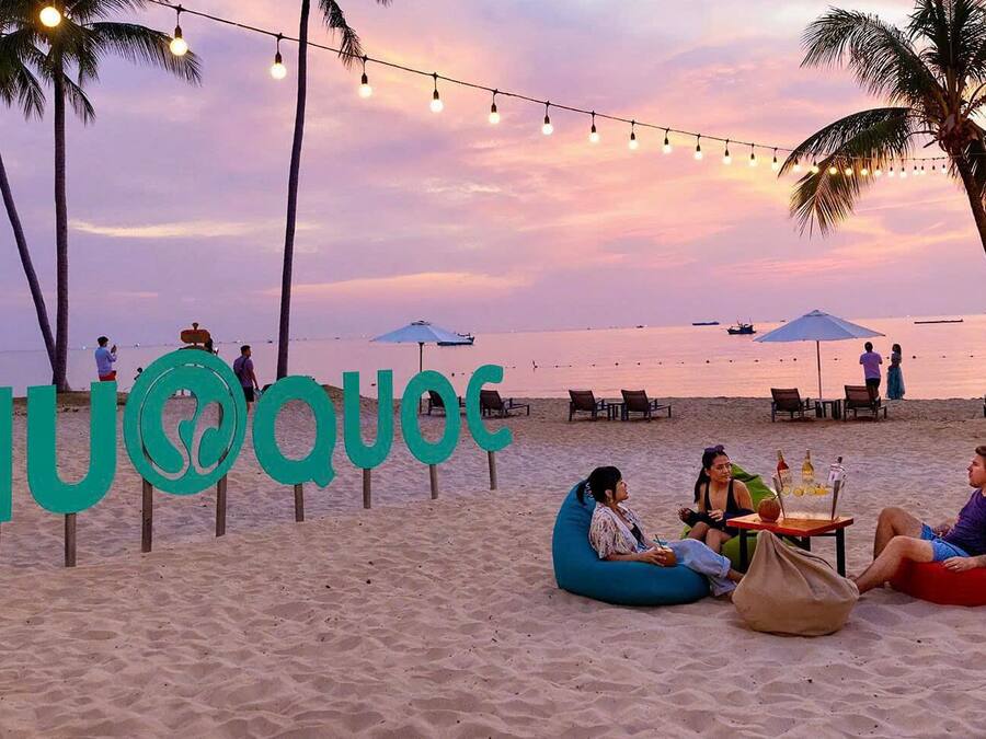 A beach scene with a sign reading "PHUQUES" and people relaxing on bean bags.