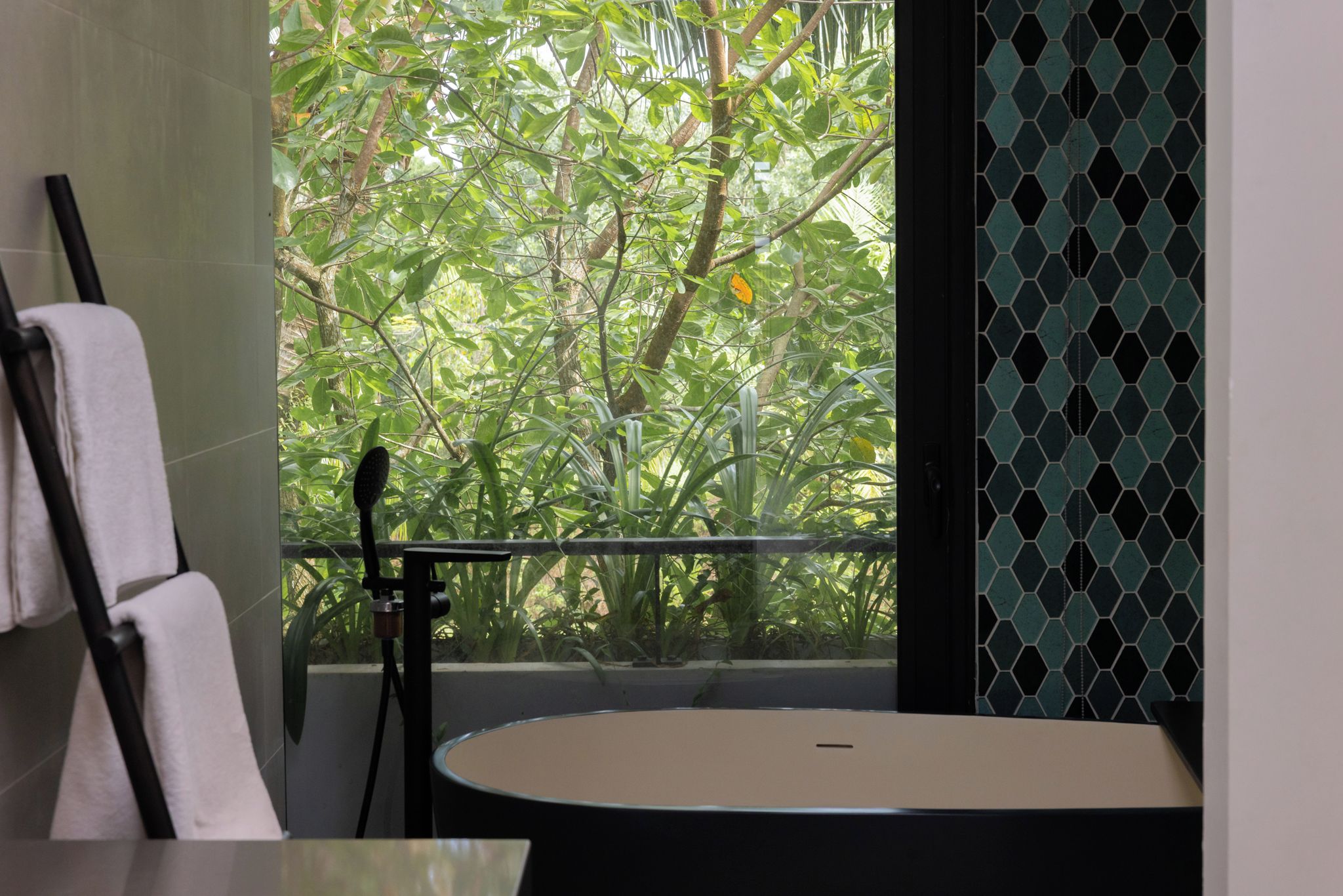 Une salle de bain avec une baignoire, un porte-serviettes et une vue sur la verdure par une fenêtre.
