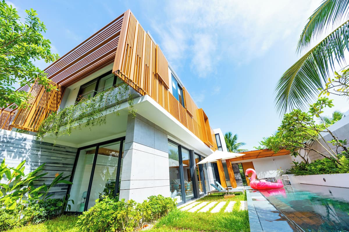 A modern house with a swimming pool, a pink flamingo float, and lush greenery.