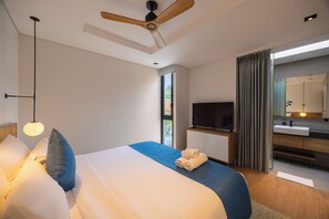 Une chambre d’hôtel moderne dotée d’un grand lit, d’un téléviseur à écran plat, d’un ventilateur de plafond en bois et d’une salle de bain avec un miroir et un lavabo.