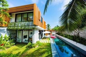 A modern house with a swimming pool, lush greenery, and a pink flamingo decoration.