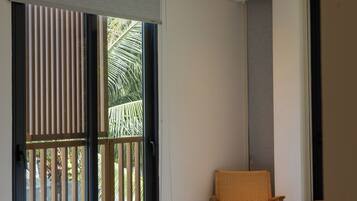 A hotel room with a bed, a ceiling fan, a window with blinds, and a view of palm trees.