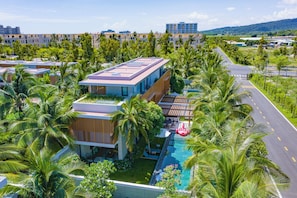 Un hotel moderno con piscina en la azotea, rodeado de exuberante vegetación y palmeras.
