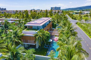 Un hotel moderno con piscina en la azotea, rodeado de exuberante vegetación y palmeras.