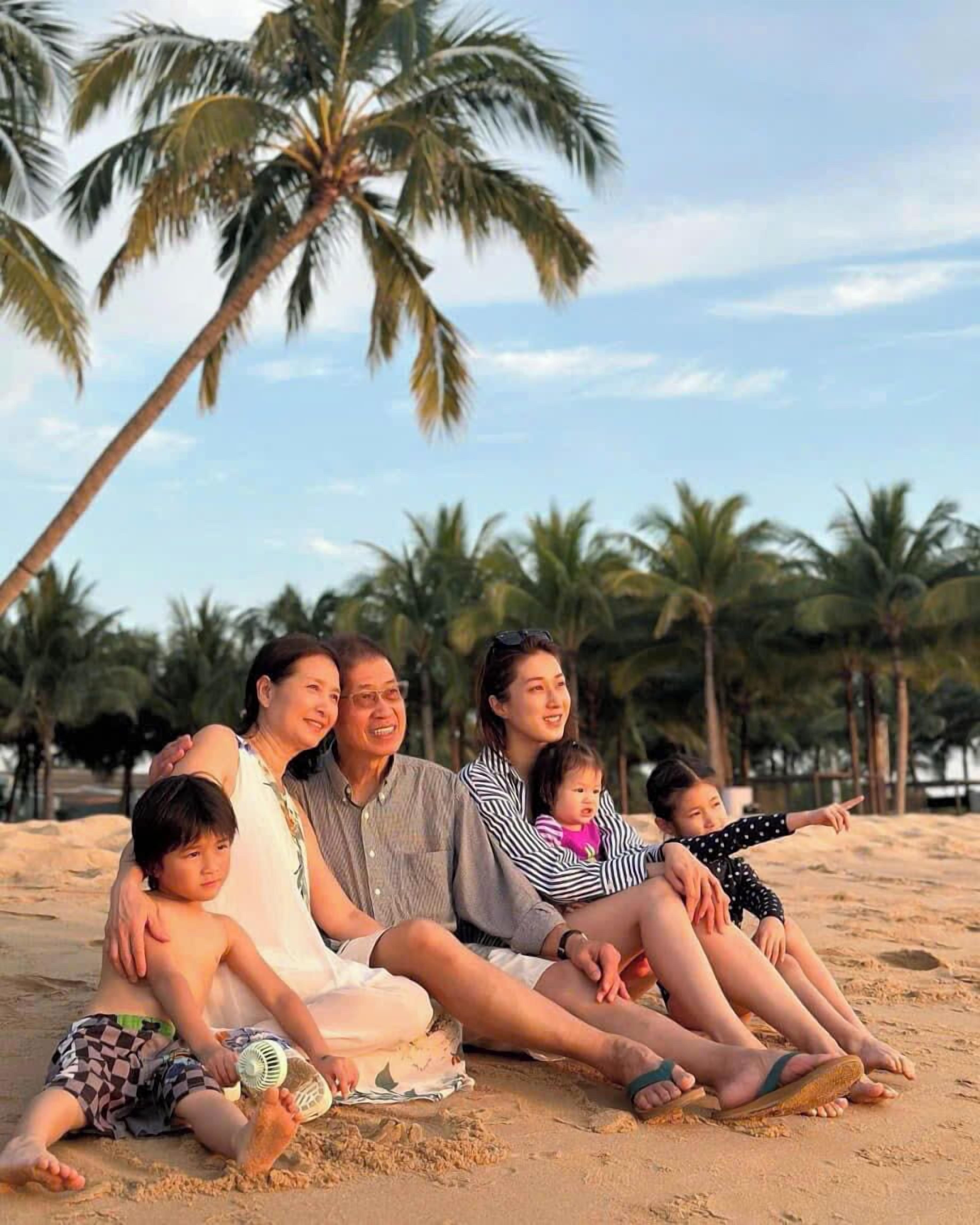 A family sitting on a sandy beach with palm trees in the background.