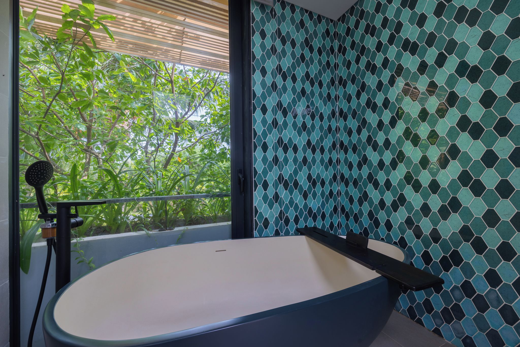 Un baño moderno con una bañera independiente, un cabezal de ducha y vistas a zonas verdes.