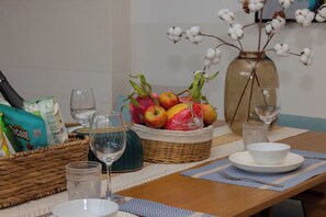 A dining table with a fruit basket, wine glasses, and a vase with cotton plants. - Sailing Pool Villas & Resort Phu Quoc (Phu Quoc)