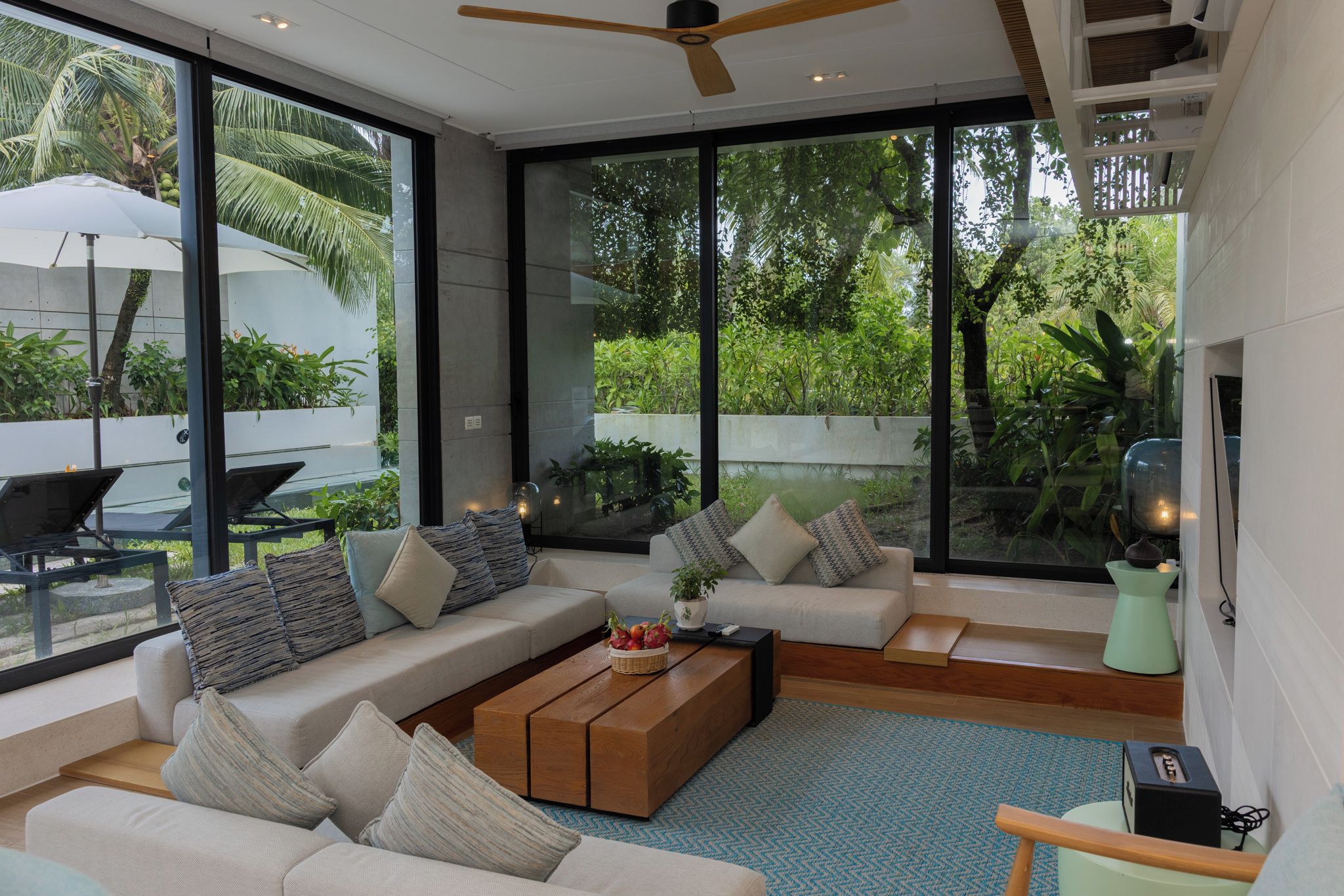 Una sala de estar moderna con un conjunto de sofá, una mesa de centro y ventanas grandes que ofrecen vistas al verdor.