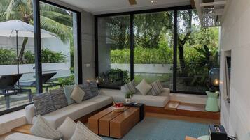 Una sala de estar moderna con un conjunto de sofá, una mesa de centro y ventanas grandes que ofrecen vistas al verdor.