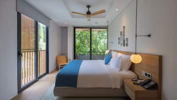 A modern bedroom with a large bed, a ceiling fan, a bedside table with a lamp, and a view of greenery through the window.