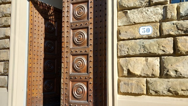 Una puerta de madera con diseños circulares y un muro de piedra con un letrero con el número 50.