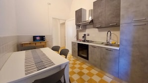 Cocina compacta con microondas, estufa, pileta y alacenas. Hay una mesa de comedor con sillas y un televisor en la esquina.