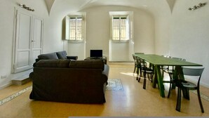 Amplia habitación con techo abovedado, un sofá, una mesa de comedor con sillas y dos ventanas.