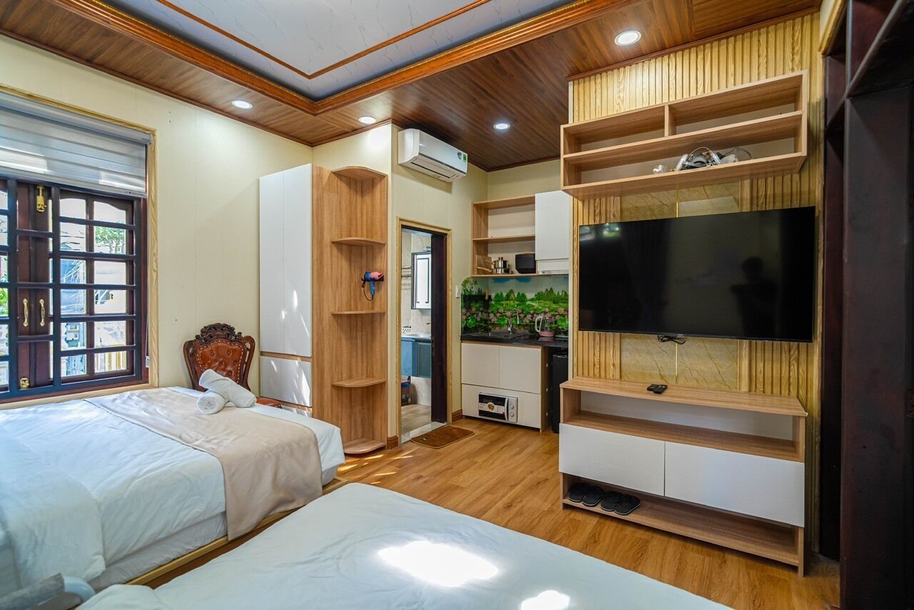 A bedroom with two beds, a TV, wooden shelving, and a kitchen area.