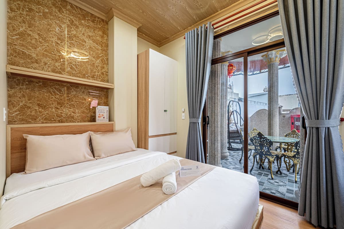 A hotel room with a bed, a note on the bed, a window with curtains, and a view of the outside.