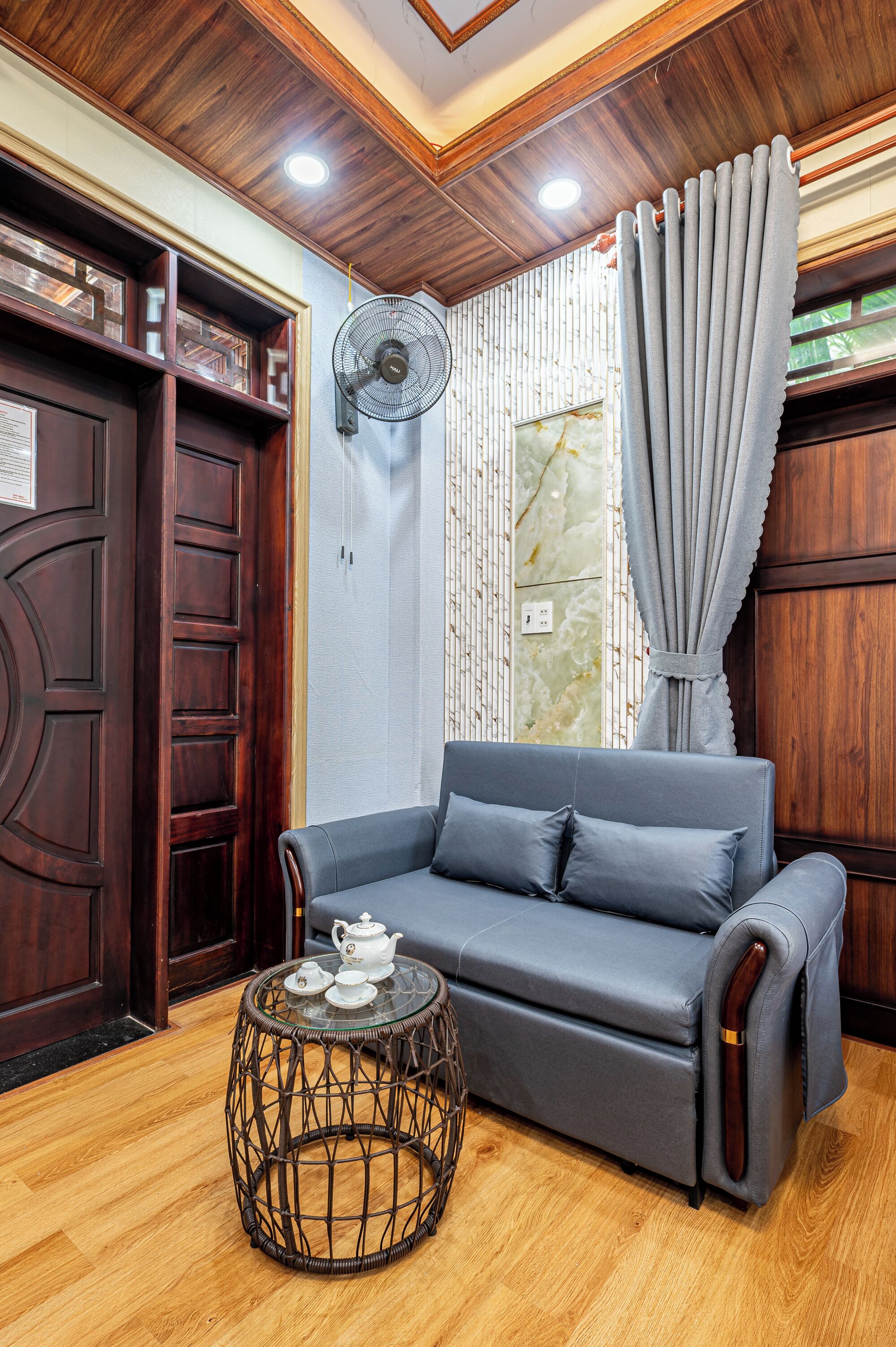 A modern living room with a grey sofa, a round wicker coffee table, and a fan on the wall.