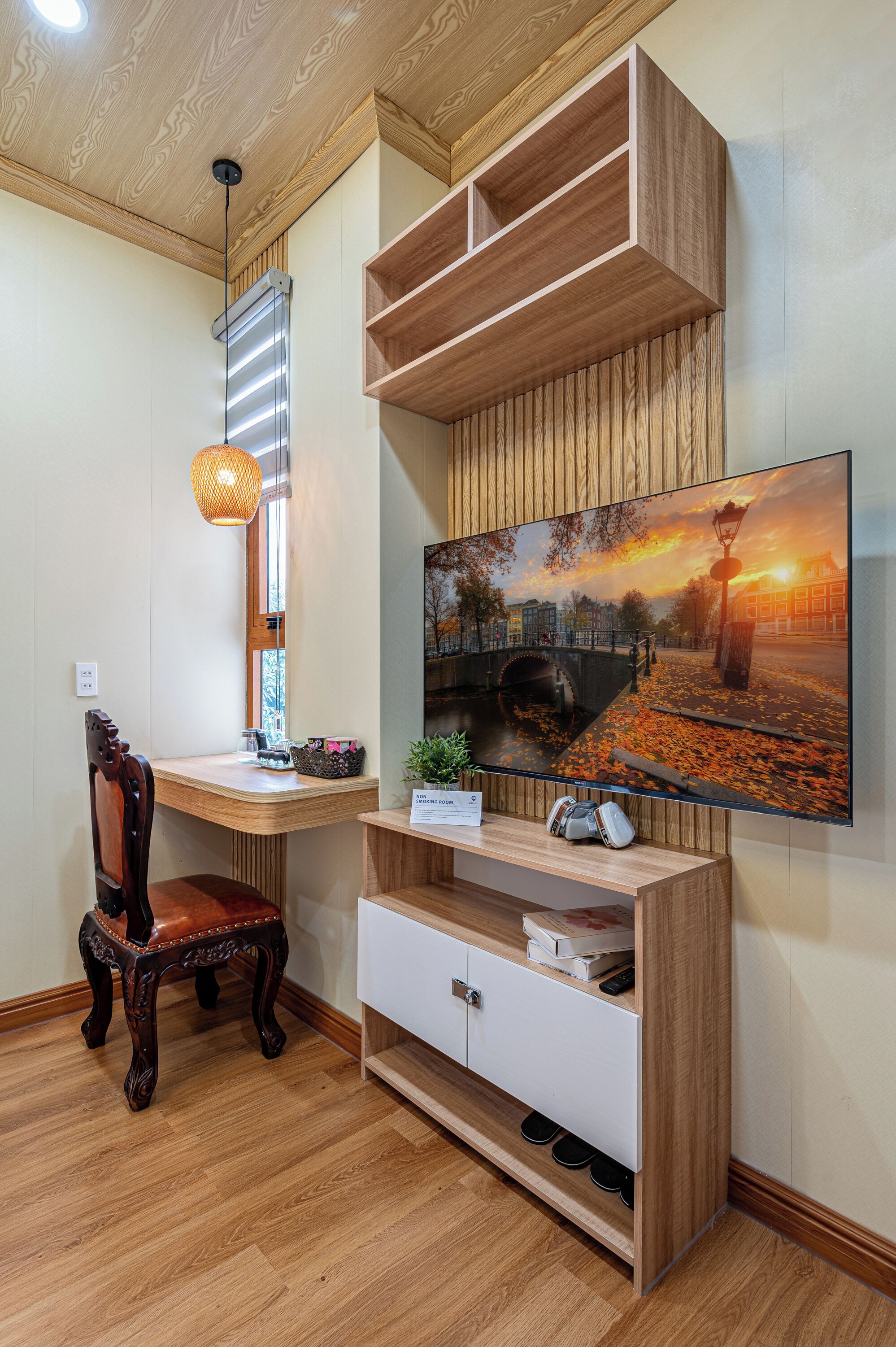Ein Zimmer mit einem Holztisch, einem Stuhl, einem an der Wand befestigten Fernseher und einem Fenster mit Jalousien.
