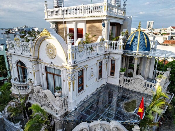 A grand building with ornate white and gold detailing, a large glass-covered courtyard, and a flag. - Cozrum - Cozy Home Phú Yên (Tuy Hoa)