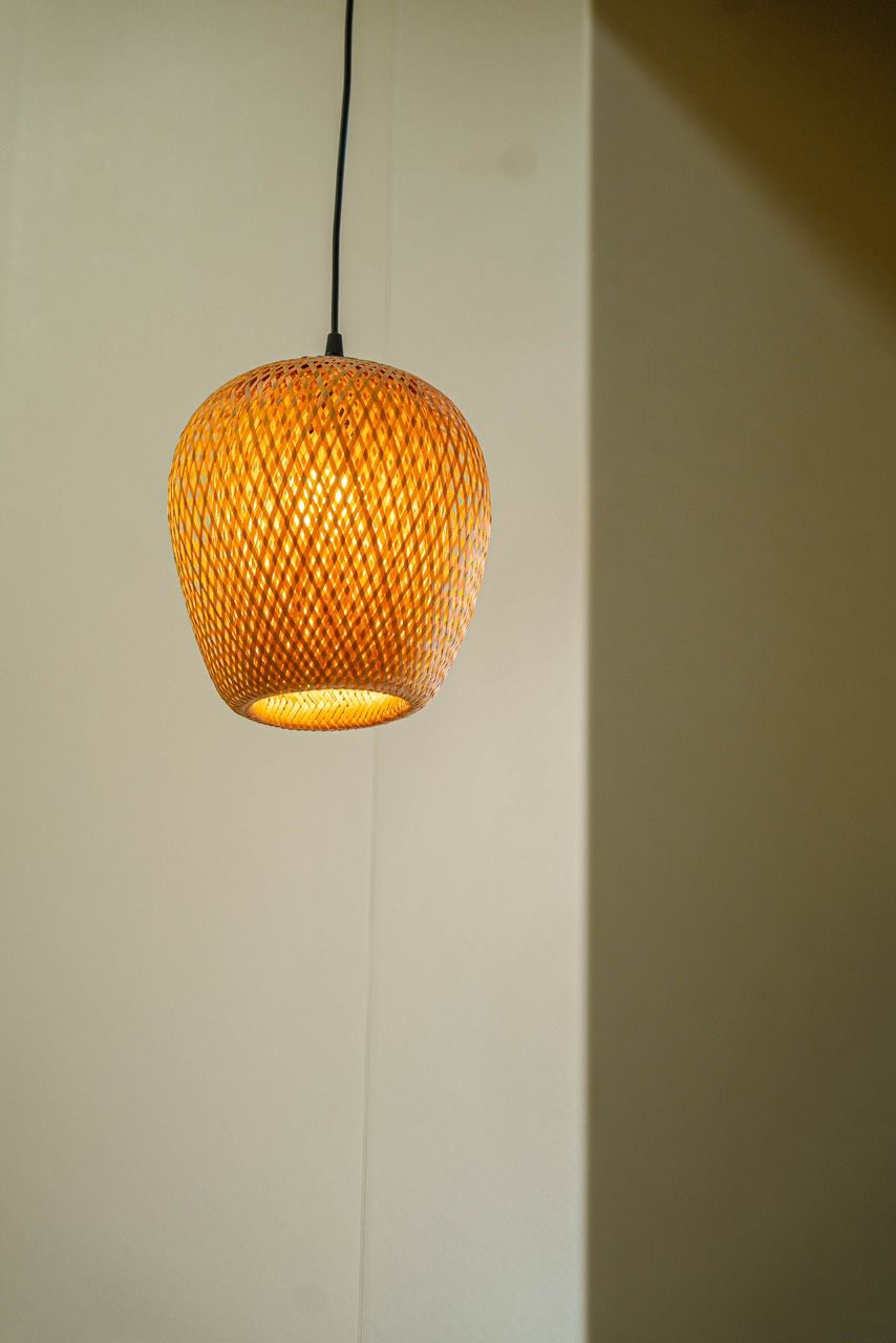 Lampada a sospensione sferica, intrecciata, appesa tramite un cavo nero su un muro neutro.