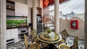 A kitchen with a modern design, including a black countertop, white cabinets, and a decorative backsplash. There is a dining area with ornate chairs and a round table, and a hanging chair with cushions. - Cozrum - Cozy Home Phú Yên (Tuy Hoa)