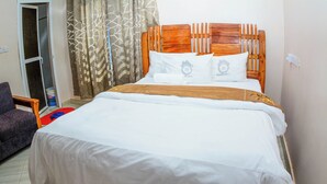 A neatly made bed with a wooden headboard, white bedding, and two pillows with a logo. - Bezinda Lodge (Dodoma)