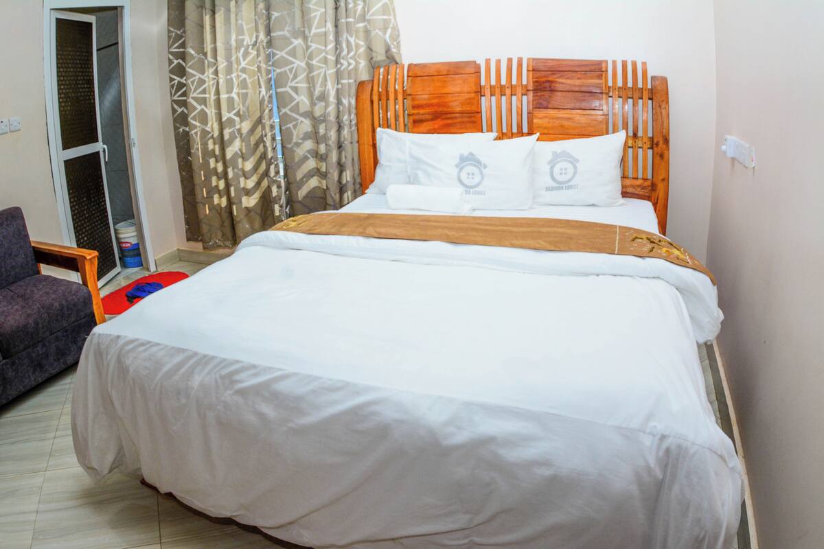 A neatly made bed with a wooden headboard, white bedding, and two pillows with a logo.