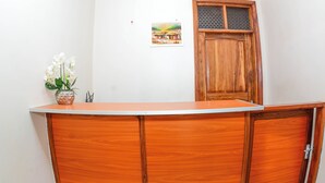 A reception desk with a wooden finish, a potted plant with white flowers, and a framed picture on the wall. - Bezinda Lodge (Dodoma)