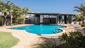 A swimming pool with a glass enclosure, surrounded by palm trees and a patio area with lounge chairs. - Beautiful Marina View Apartment (Geraldton)