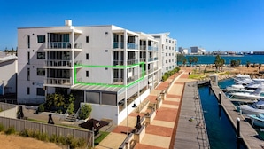 A modern multi-story hotel with balconies, a marina with boats, and a clear view of the sea. - Beautiful Marina View Apartment (Geraldton)