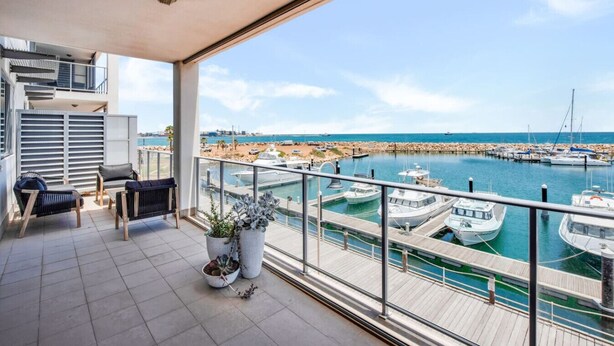 A balcony with a view of a marina, outdoor seating, and a potted plant. - Beautiful Marina View Apartment (Geraldton)