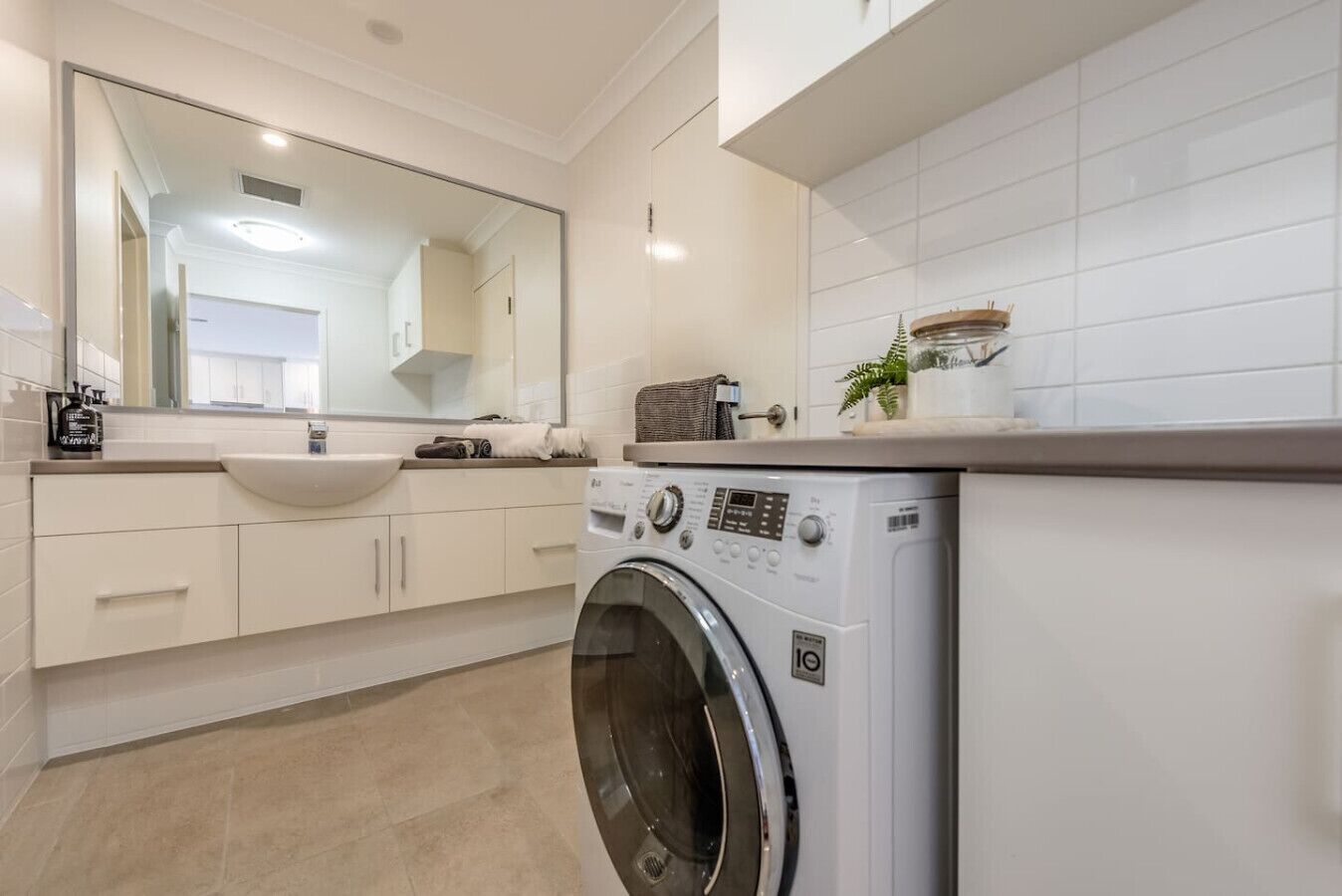 A modern bathroom with a large mirror, a sink, a washing machine, and a toilet.