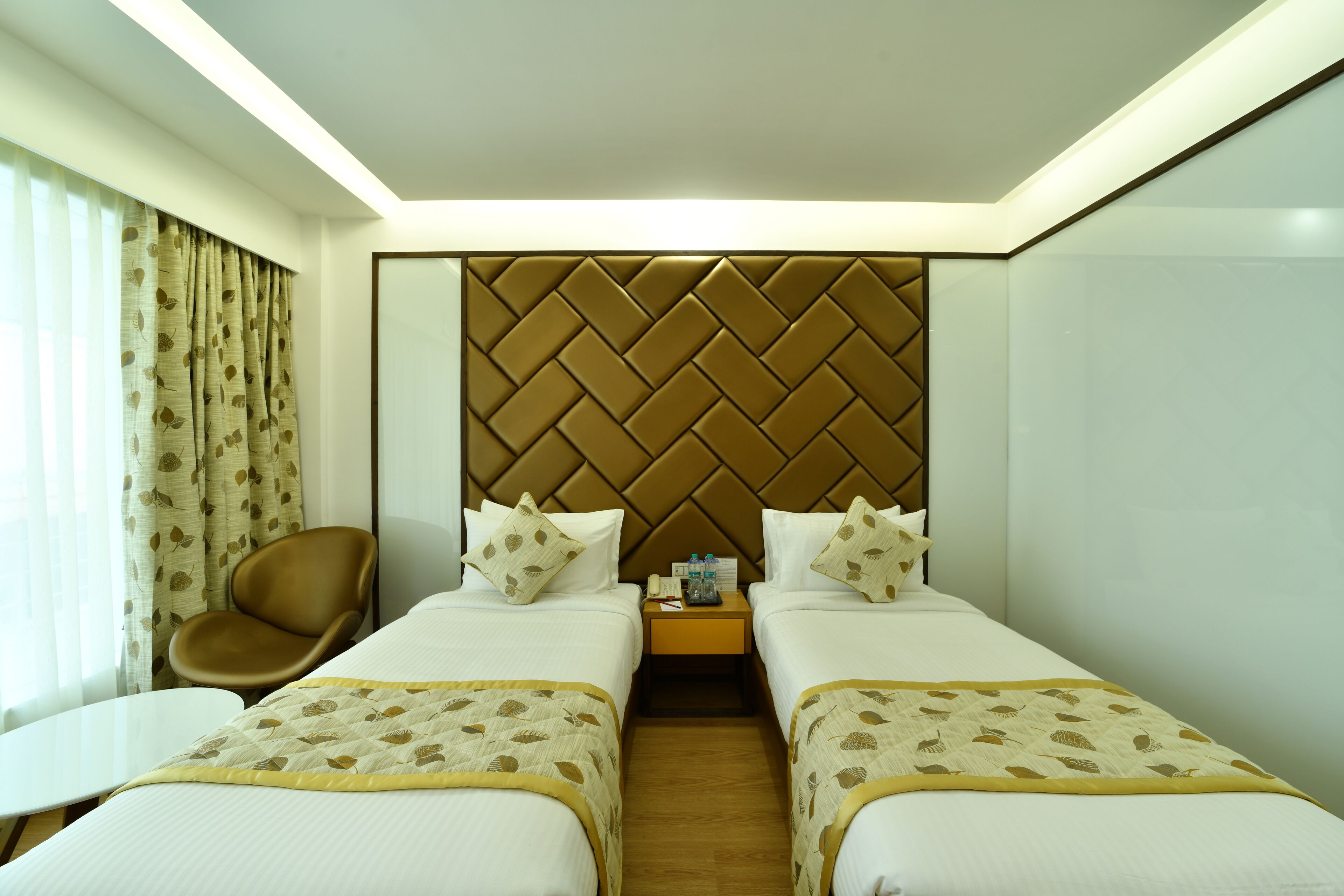 A hotel room with two beds, a chair, a small table, and a nightstand with a lamp.