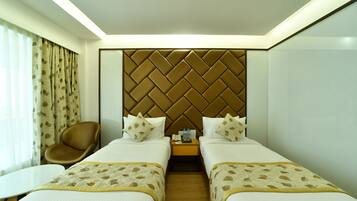 A hotel room with two beds, a chair, a small table, and a nightstand with a lamp.