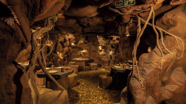 Un restaurant souterrain où les tables sont disposées contre les parois de la grotte, éclairées par un éclairage d’ambiance.