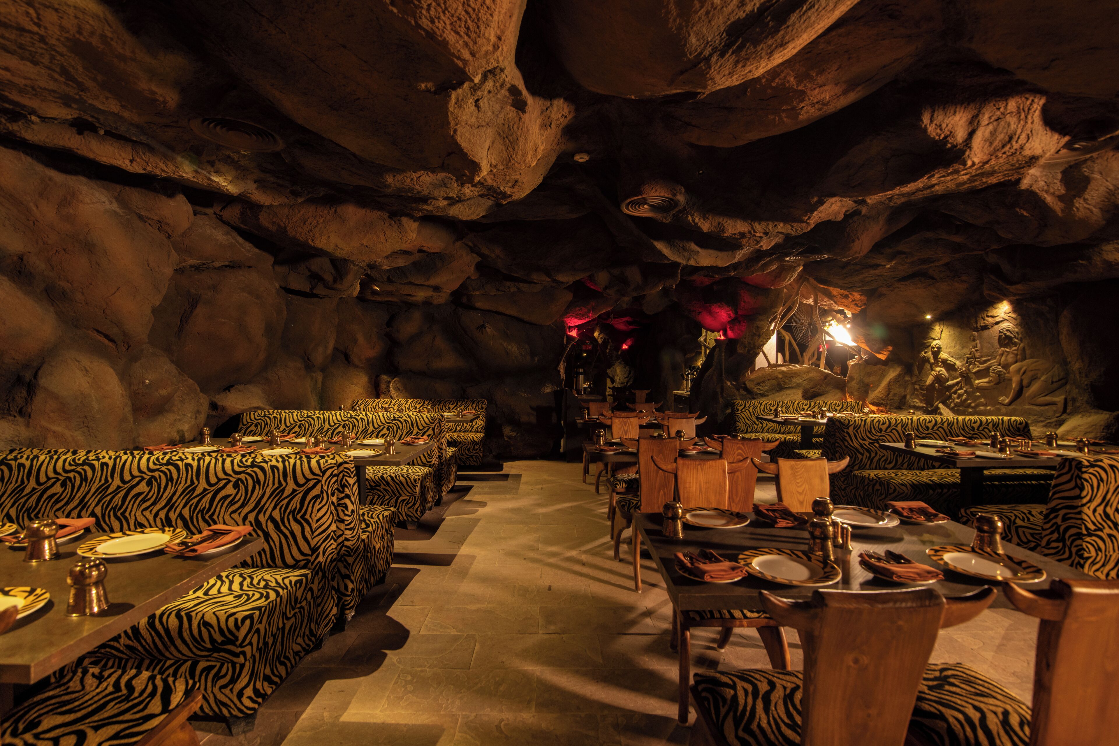 An interior with zebra-striped seating and tables, set against a cave-like backdrop with rock formations.
