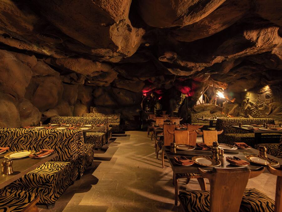 An interior with zebra-striped seating and tables, set against a cave-like backdrop with rock formations.