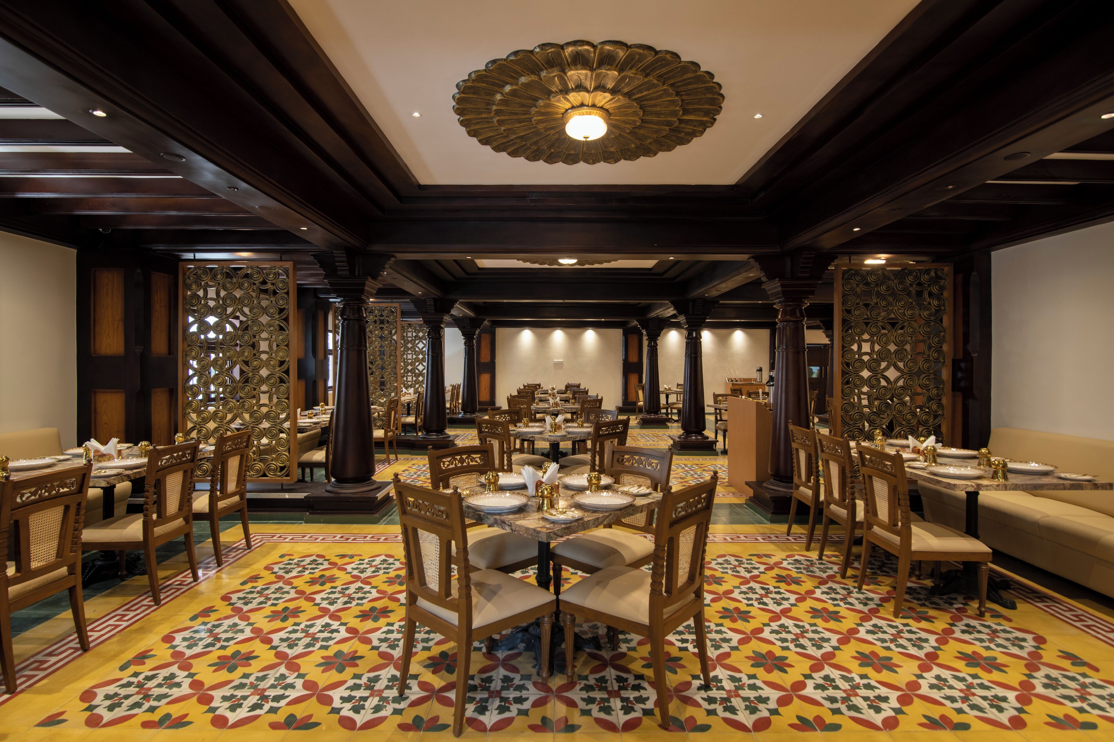 A spacious dining area with multiple tables and chairs, ornate ceiling design, and patterned floor tiles.