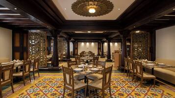 Un comedor espacioso con múltiples mesas y sillas, un diseño de techo ornamentado y baldosas de suelo estampadas.