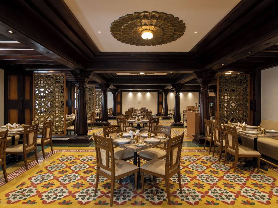 Un comedor espacioso con múltiples mesas y sillas, un diseño de techo ornamentado y baldosas de suelo estampadas.