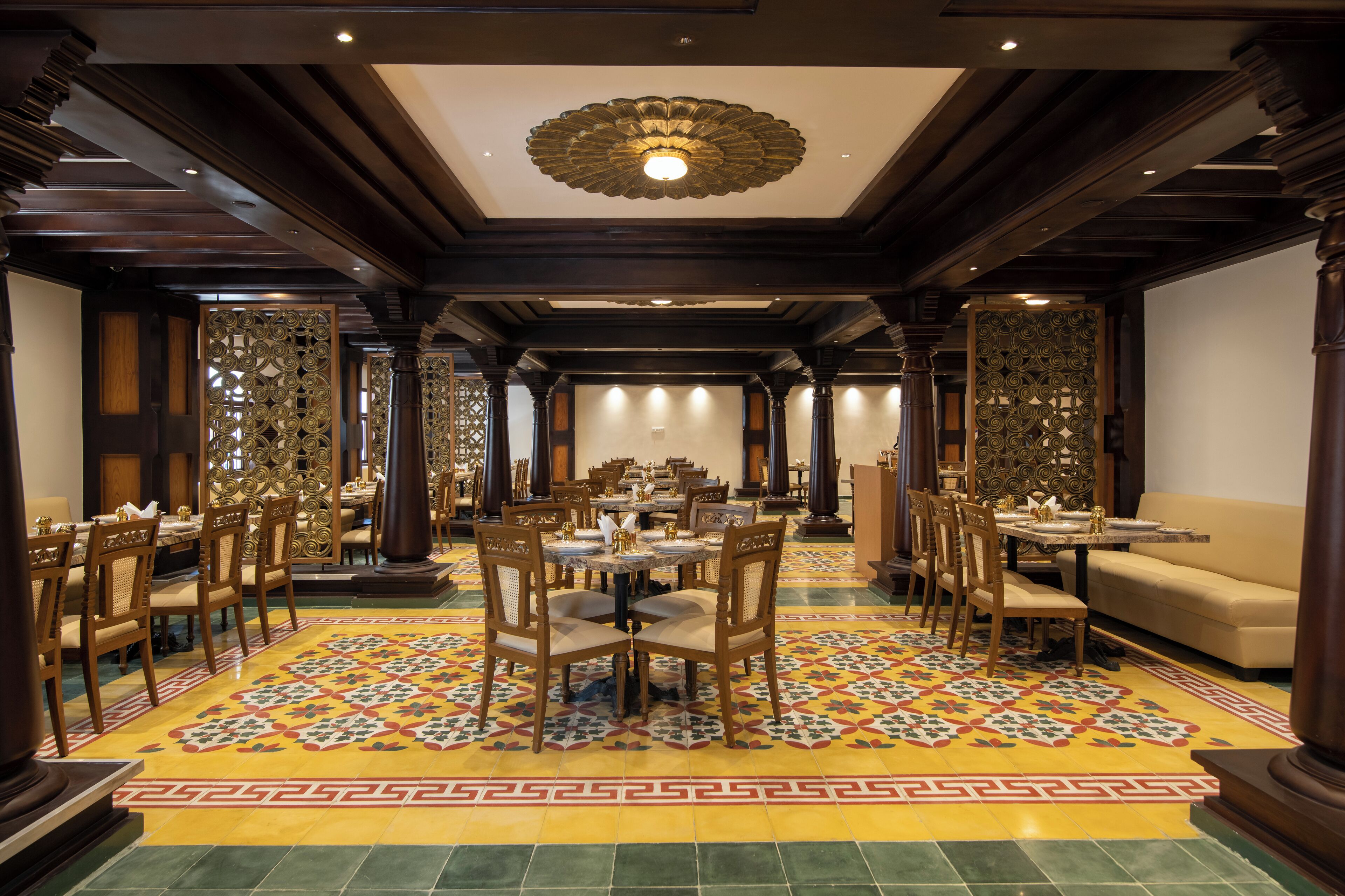 A spacious dining area with multiple tables and chairs, a patterned floor, and a decorative ceiling light.