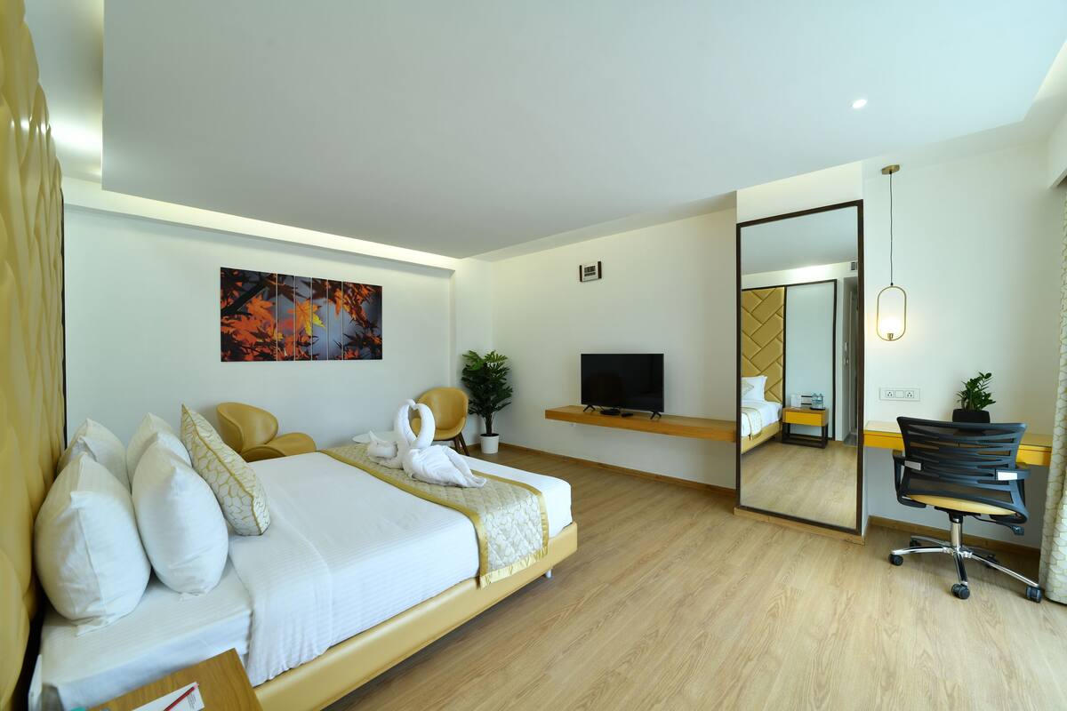 Een moderne hotelkamer met een bed, een bureau, een stoel, een televisie, een spiegel en een potplant.
