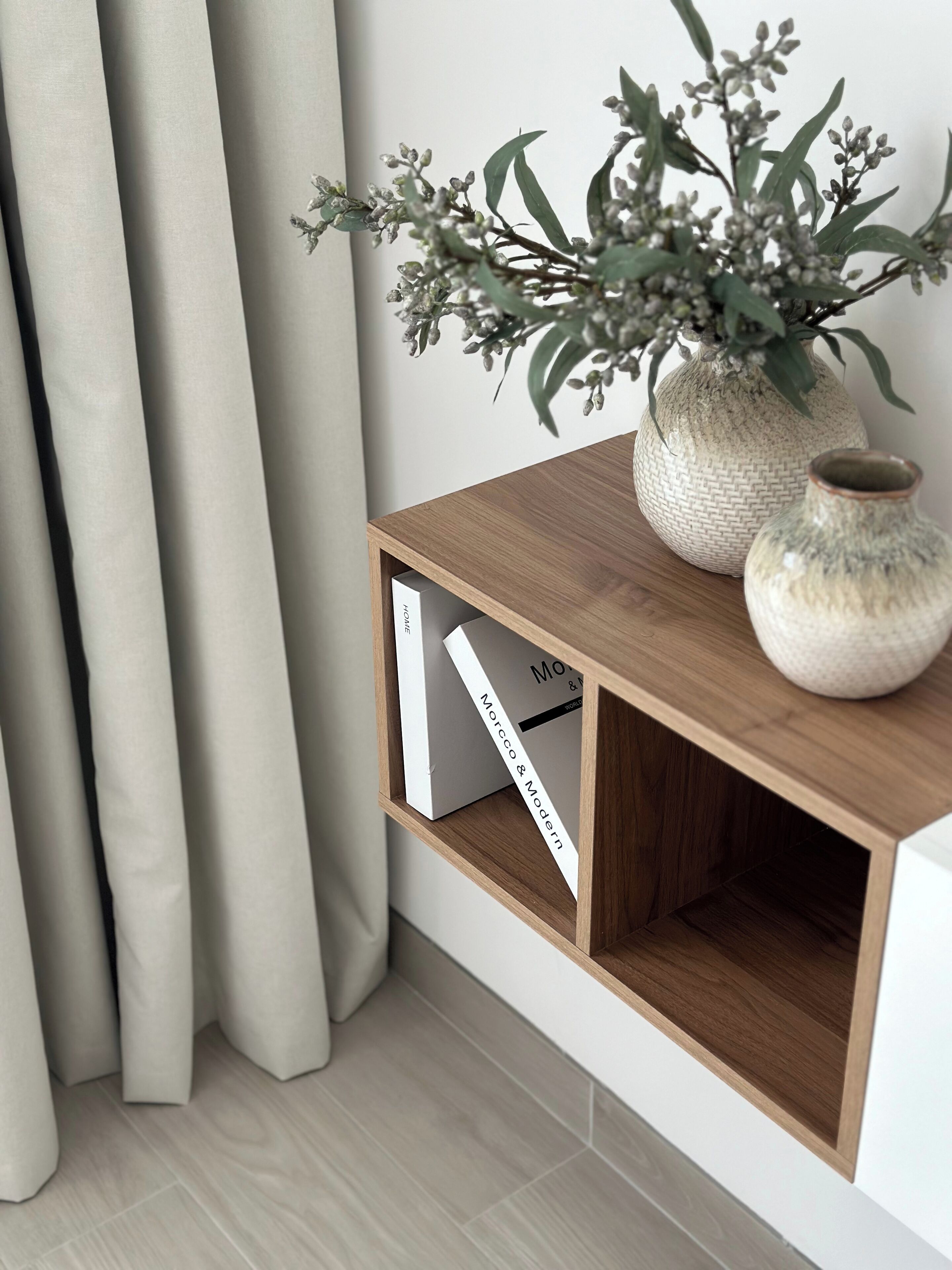 A corner of a room with a wooden shelf, a vase with greenery, and a book titled "Morcco & Modern".