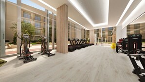 Une salle de sport moderne équipée de machines de cardio, de postes d’entraînement avec poids et d’un grand mur vitré qui laisse entrer la lumière naturelle.