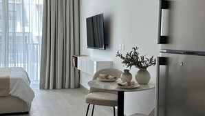 Un salon moderne et minimaliste, doté d’un grand lit, d’un coin repas avec une table et des chaises, d’un téléviseur encastré et d’un grand réfrigérateur.