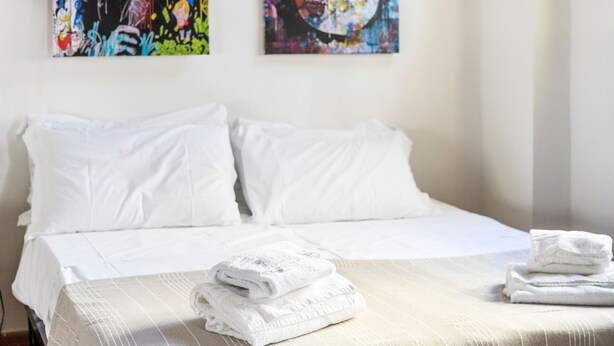 A hotel room with a bed, white linens, and two abstract paintings on the wall. - Ghibellina Loft in Firenze (Florence)