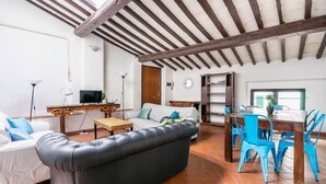 A living room with a sofa, a dining table with chairs, a television, and a ceiling with exposed beams. - Ghibellina Loft in Firenze (Florence)