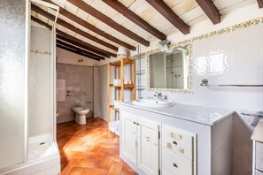 Une salle de bain avec douche, toilettes et lavabo, des poutres en bois au plafond et un sol carrelé.